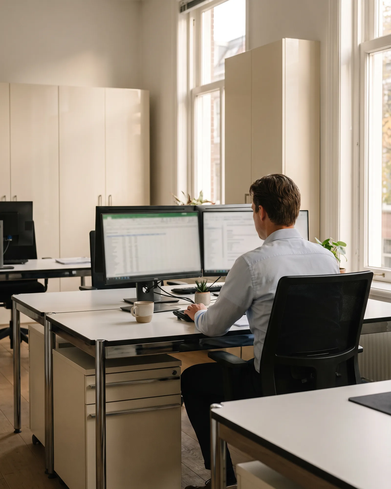 Een calculator van ons werkt aan een bureau met twee schermen vol begrotingsregels