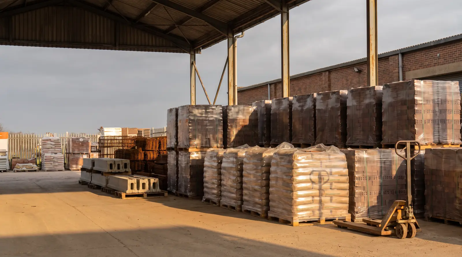 Pallets met stenen, mortel, wapening en prefab lateien klaar onder de overkapping van een bouwmaterialenwerf