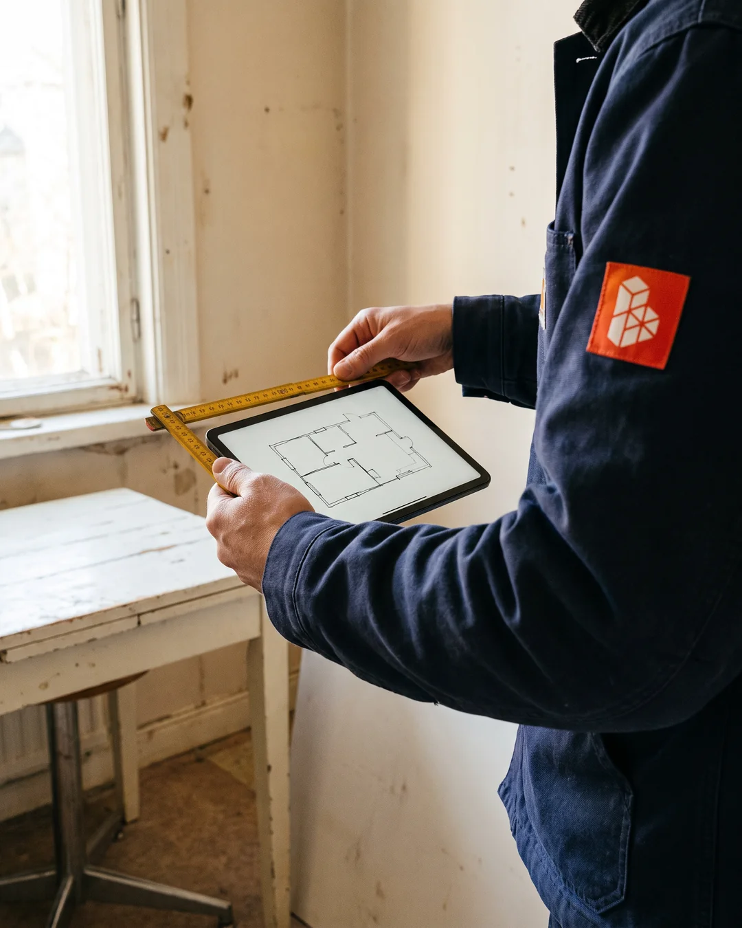Handen met een duimstok en een tablet bij een wand die open gaat