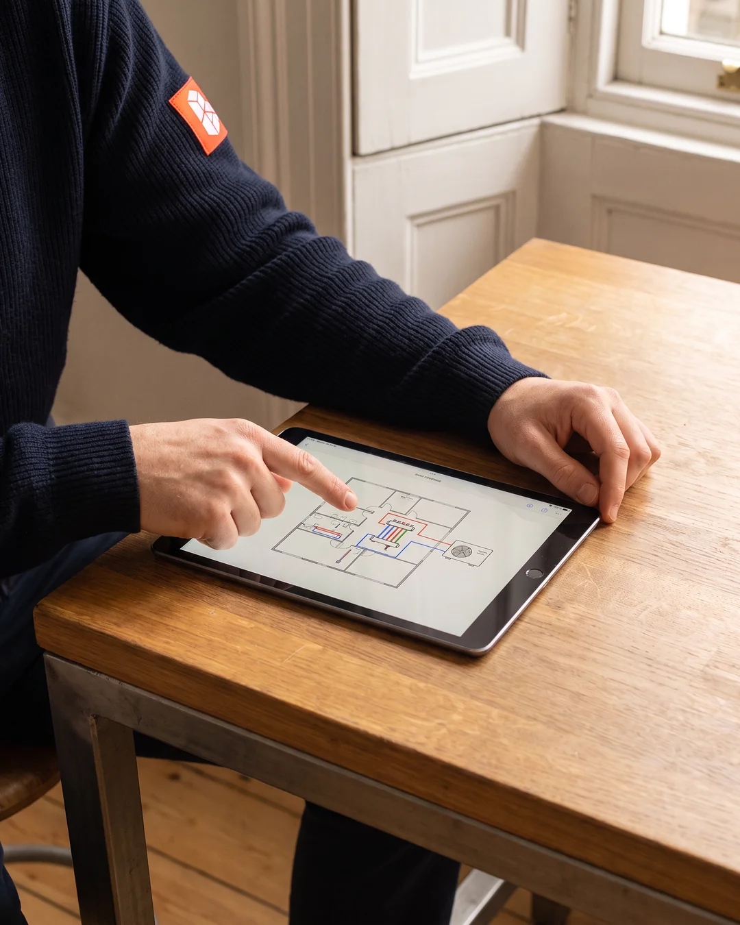 Handen die op een tablet het installatieplan aanwijzen, met de leidingen en de plek van de buitenunit