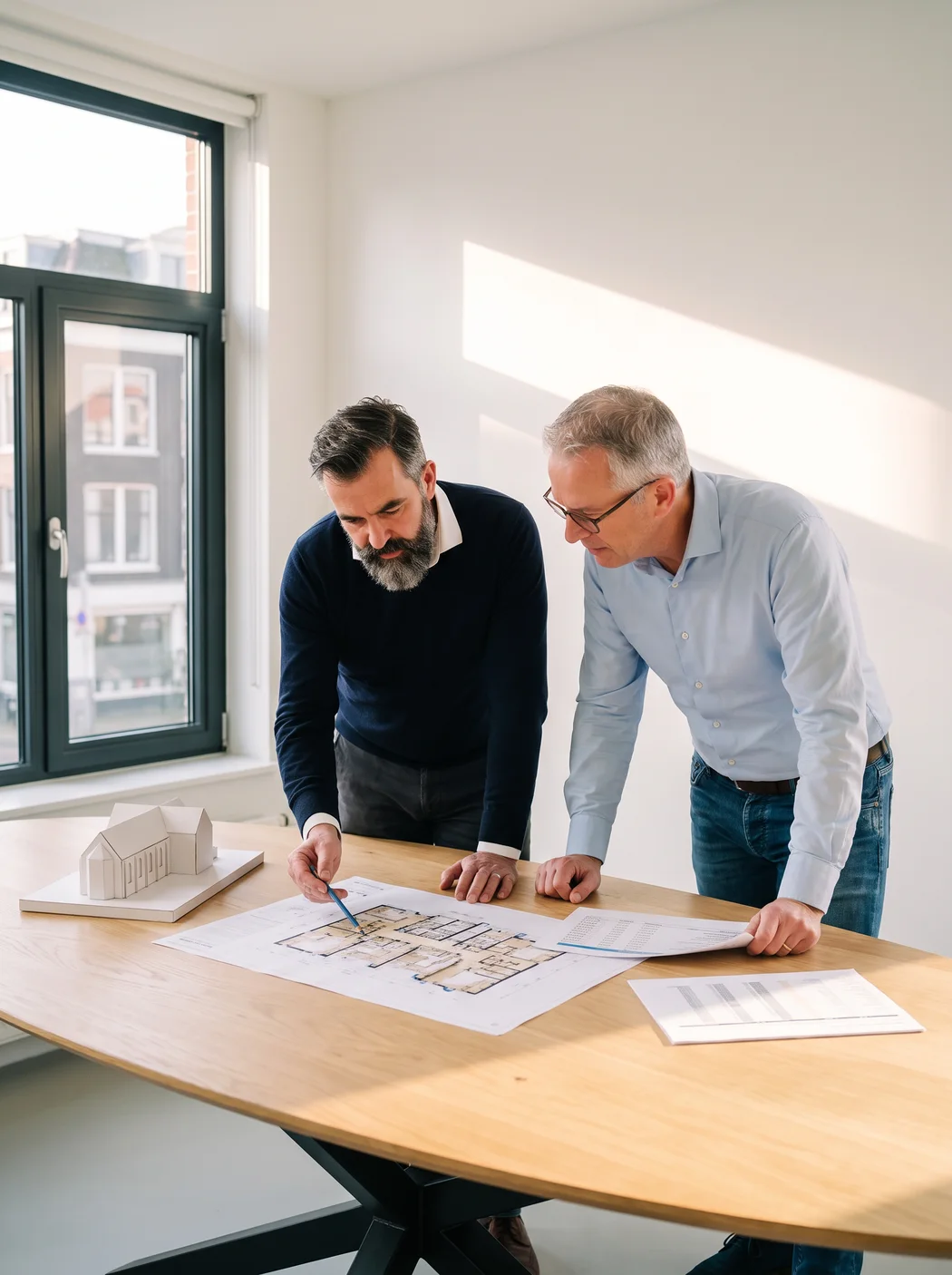 Een architect en een rekenaar van ons bekijken aan een werktafel een situatietekening en een begroting van een voormalige kerk die woningen wordt